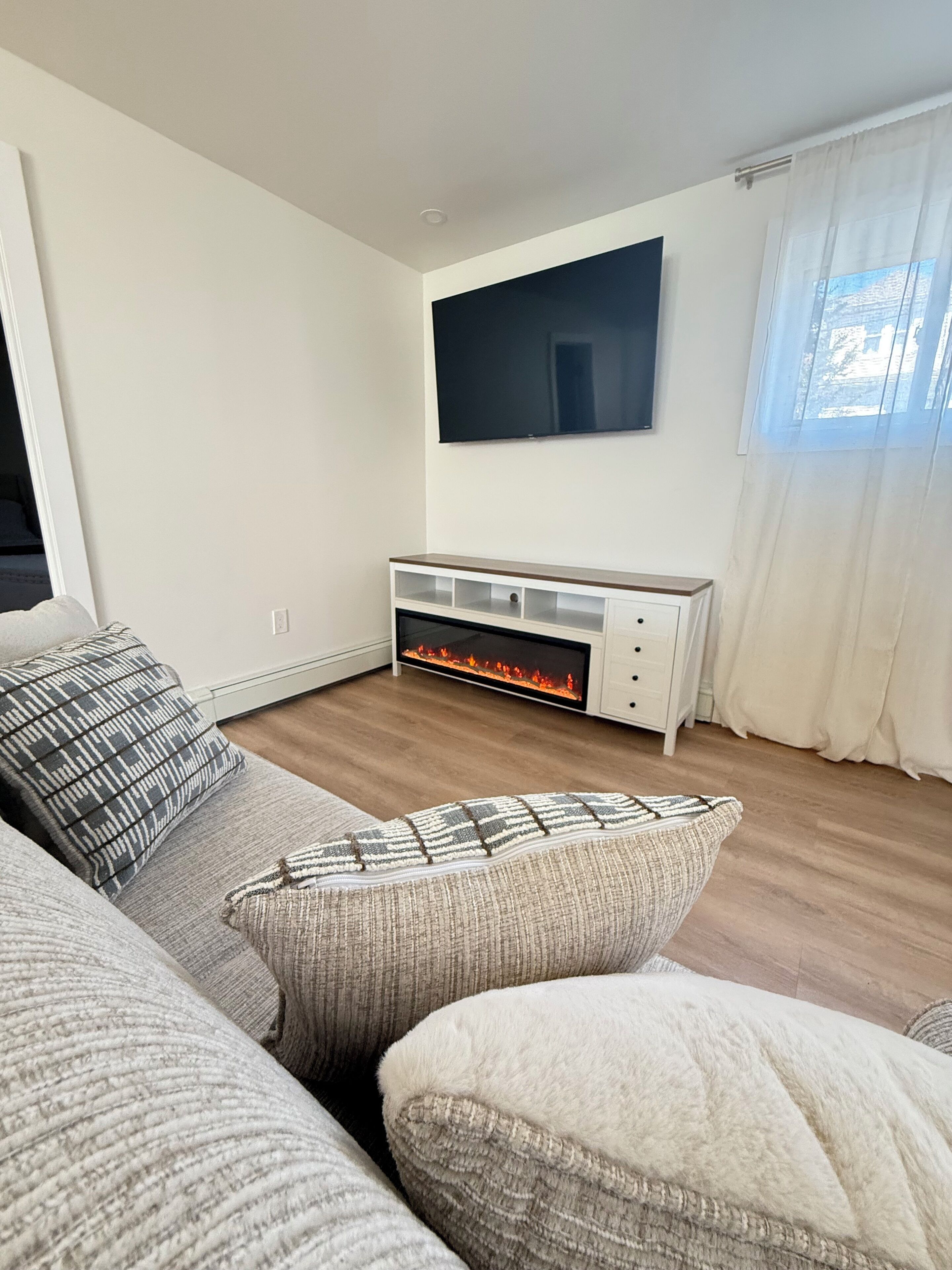 Ein Wohnzimmer mit Kamin, einem flachbildfernseher an der Wand und einer Couch mit gemusterten Kissen.