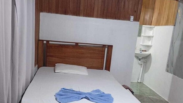 Una cama individual con cabecera de madera, sábanas blancas y una toalla azul.