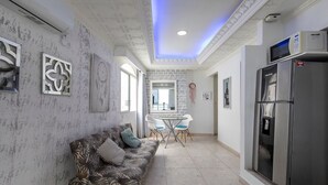 Una cocina moderna con refrigerador integrado, un área de comedor con mesa y sillas de vidrio, y un sofá estampado.