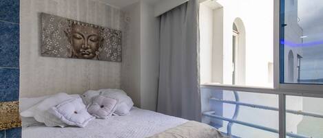 A bedroom with a bed, a large window, and a view of a building.