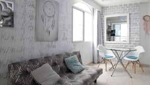 Una sala de estar con un sofá estampado, una mesa de comedor con sillas y una cocina visible a través de una puerta abierta.