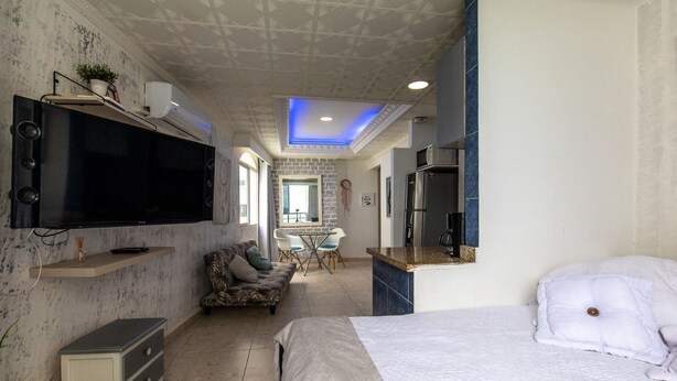 Una habitación de hotel moderna con televisión de pantalla plana, sofá, cama, pequeña cocina y mesa de comedor.
