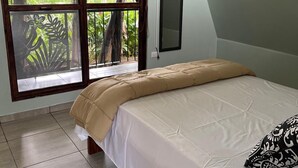 A bedroom with a bed, a TV mounted on the wall, and a window with a view of greenery. - Las Casitas italiana (Sabalito)