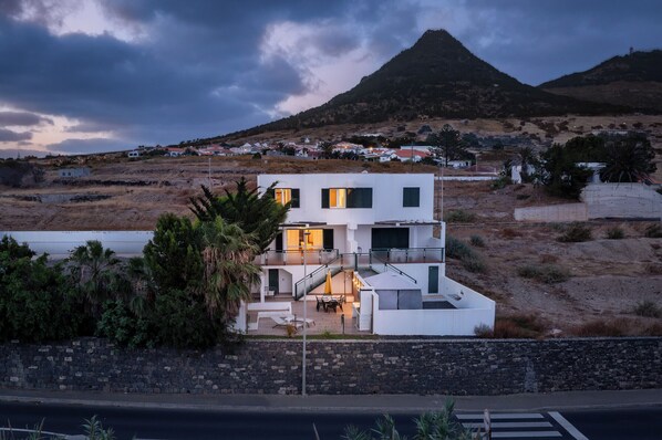 Une maison moderne à deux étages, dotée d’un balcon, située dans une région vallonnée offrant une vue sur le paysage.