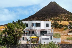 Un bâtiment moderne à deux étages, doté d’un balcon, entouré de verdure et avec une montagne en arrière-plan.