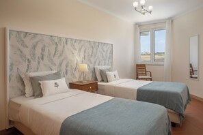 Une chambre avec deux lits, une table de chevet, une chaise et une fenêtre donnant sur un beau paysage.