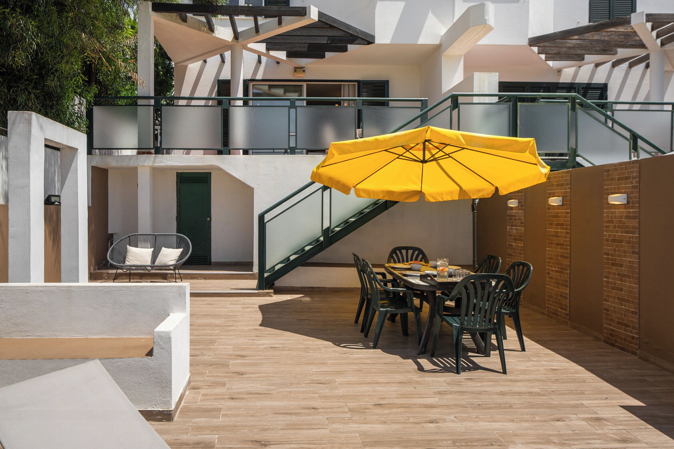Un patio al aire libre con una mesa y sillas para comer, un paraguas amarillo y una escalera.