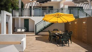 Un patio al aire libre con una mesa y sillas para comer, un paraguas amarillo y una escalera.