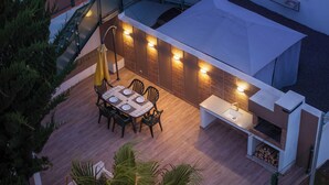 An outdoor patio with a table and chairs, a built-in barbecue, and a pergola with lights.