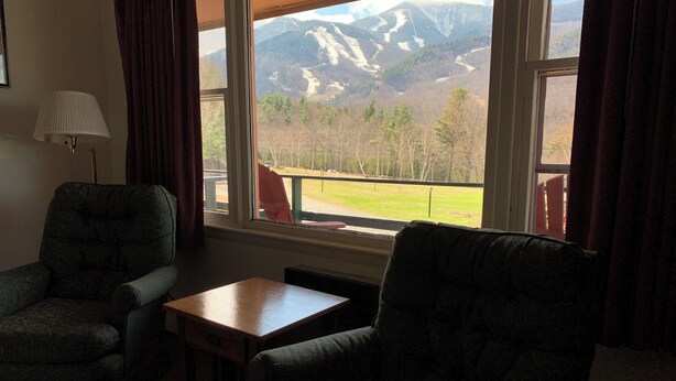 Una habitación con vista a las montañas, una mesa, dos sillones y una lámpara.