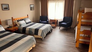 Habitación de hotel con dos camas, una litera de madera, un escritorio, dos sillas y una ventana con cortinas.