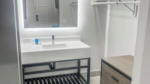 A modern bathroom with a white sink, mirror, and wooden cabinet. - Value Suites Extended Stay (Sacramento)