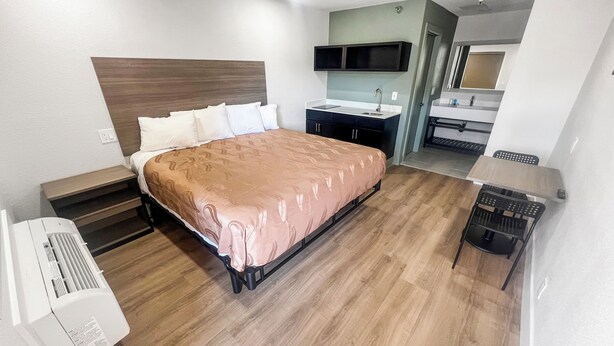 A hotel room with a bed, bedside tables, a desk, a chair, a TV, and a bathroom with a sink and mirror. - Value Suites Extended Stay (Sacramento)