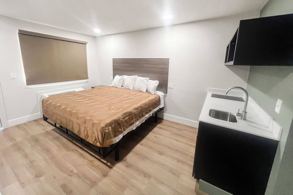A bedroom with a bed, a window with blinds, a bedside table, and a built-in sink.