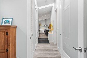 A hallway leading to a kitchen with a wooden cabinet and a framed picture on the left.