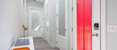 A hallway with a white door, a red door, and a small table with a lamp and magazines.