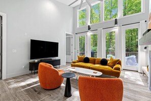 A modern living room with a large flat-screen TV, a mustard-colored sofa with black cushions, and two orange armchairs.