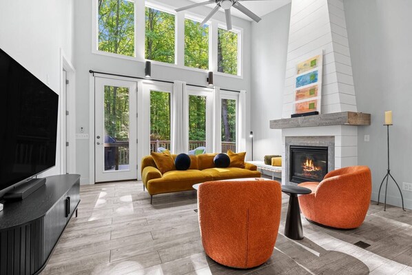 A modern living room with a large TV, orange chairs, a sofa, and a fireplace.