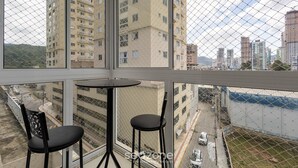 Ein Balkon mit zwei schwarzen Stühlen und einem kleinen Tisch, mit Blick auf eine Stadtlandschaft mit mehreren Hochhäusern und einer Straße.