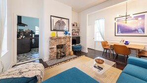 A living room with a fireplace, a dining area with a table and chairs, and a kitchen in the background.
