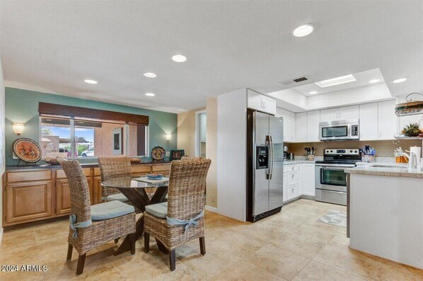 A modern kitchen with white cabinetry, stainless steel appliances, and a dining area with wicker chairs.