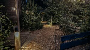 A pathway leading to a wooden building with string lights, surrounded by dense foliage.