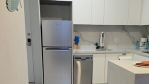 A modern kitchen with white cabinets, a stainless steel refrigerator, a dishwasher, and a marble countertop. - Chic 1-bedroom luxury suite in fabulous Nassau. Comfort. Class. Convenience. (Nassau)
