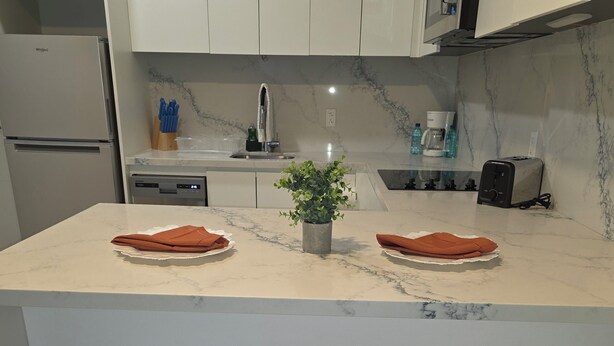 A modern kitchen with white cabinets, a marble countertop, two stools, a potted plant, and a toaster. - Chic 1-bedroom luxury suite in fabulous Nassau. Comfort. Class. Convenience. (Nassau)