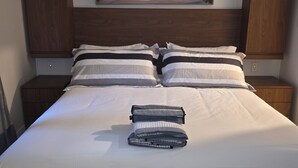 A neatly made bed with a striped pillow set, a folded towel, and a painting of a coastal walkway above it. - Chic 1-bedroom luxury suite in fabulous Nassau. Comfort. Class. Convenience. (Nassau)