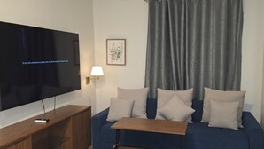 A living room with a flat-screen TV, a wooden coffee table, a blue sofa with cushions, a lamp, and a framed picture on the wall. - Chic 1-bedroom luxury suite in fabulous Nassau. Comfort. Class. Convenience. (Nassau)