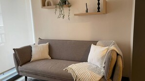 Ein Wohnzimmer mit grauem Sofa, weißen Kissen, einer gestreiften Decke und zwei Holzregalen mit Dekoration.