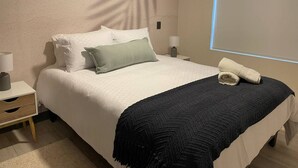 Ein ordentlich gemachtes Bett mit weißen und grünen Kissen, einer dunklen Tagesdecke und einem gefalteten Handtuch daneben.