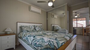 A bedroom with a bed, a nightstand, a lamp, a ceiling fan, and a large mirror.