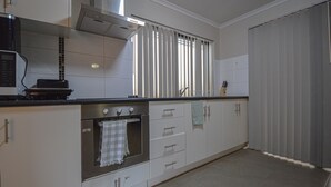 A kitchen with white cabinets, a stainless steel oven, a microwave, and a window with vertical blinds.