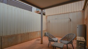 A covered outdoor area with two wicker chairs and a small table, a metal pole, and a water heater.