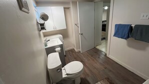 A bathroom with a toilet, sink, and mirror. There is a towel rack with two towels. The floor is wooden.