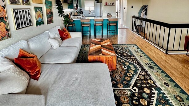 A modern living room with a sofa, a patterned rug, and a ceiling fan. - Stylish Ocean Beach Townhouse - Walk to the Sand, Relax in Comfort (San Diego)