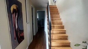 A hallway with wooden flooring, a staircase with a black railing, and a painting on the wall. - Stylish Ocean Beach Townhouse - Walk to the Sand, Relax in Comfort (San Diego)