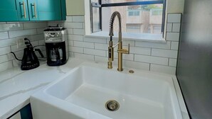 A kitchen with teal cabinets, a white sink, a coffee maker, and a window with a view of buildings. - Stylish Ocean Beach Townhouse - Walk to the Sand, Relax in Comfort (San Diego)