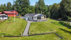 A house with a paved driveway leading to a covered porch, surrounded by lush greenery and a red barn in the background. - Awesome home in Värnamo with lake view (Värnamo)