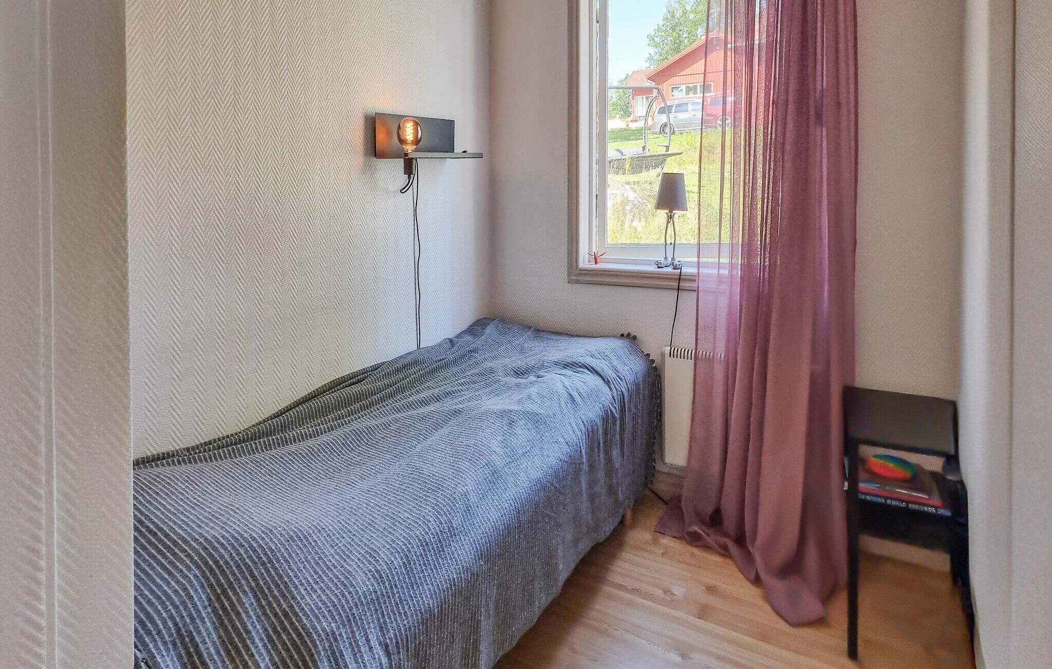 A small, neatly arranged bedroom with a single bed, a bedside table, a lamp, and a window with curtains.