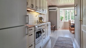 A kitchen with white cabinets, a stove, and a coffee maker. There is a window with a view of trees. - Awesome home in Värnamo with lake view (Värnamo)