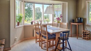 A dining area with a wooden table and chairs, large windows with plants, and a small table with bottles. - Awesome home in Värnamo with lake view (Värnamo)