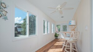 A spacious room with large windows, a ceiling fan, and a dining area with wicker chairs and a table. - 5485-Hammerhead Harbour, Old Nags Head Cove | Pet-Friendly Coastal Escape (Nags Head)