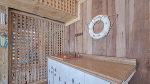 A wooden cabin with a wooden lattice door, a wooden counter with a sink, and a life ring on the wall. - 5485-Hammerhead Harbour, Old Nags Head Cove | Pet-Friendly Coastal Escape (Nags Head)