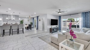 Eine moderne Küche mit Essbereich, ein Wohnzimmer mit Sofa und Fernseher sowie ein Balkon mit Vorhängen.