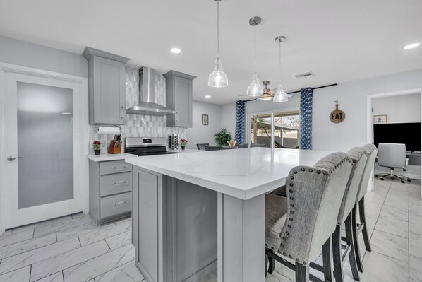 Une cuisine moderne dotée d’un grand îlot central, de meubles de rangement gris, de luminaires suspendus et d’un coin repas avec des chaises.