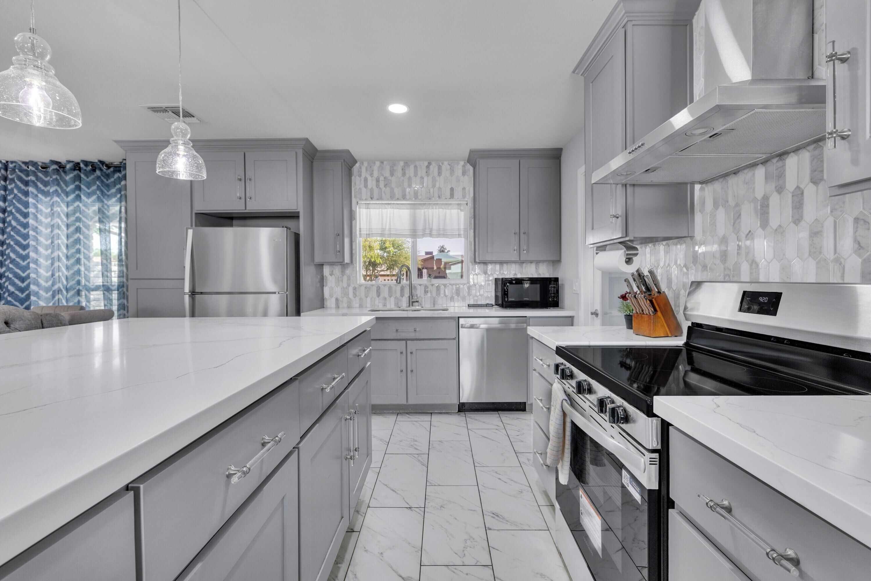 A modern kitchen with stainless steel appliances, white cabinetry, and a marble floor.