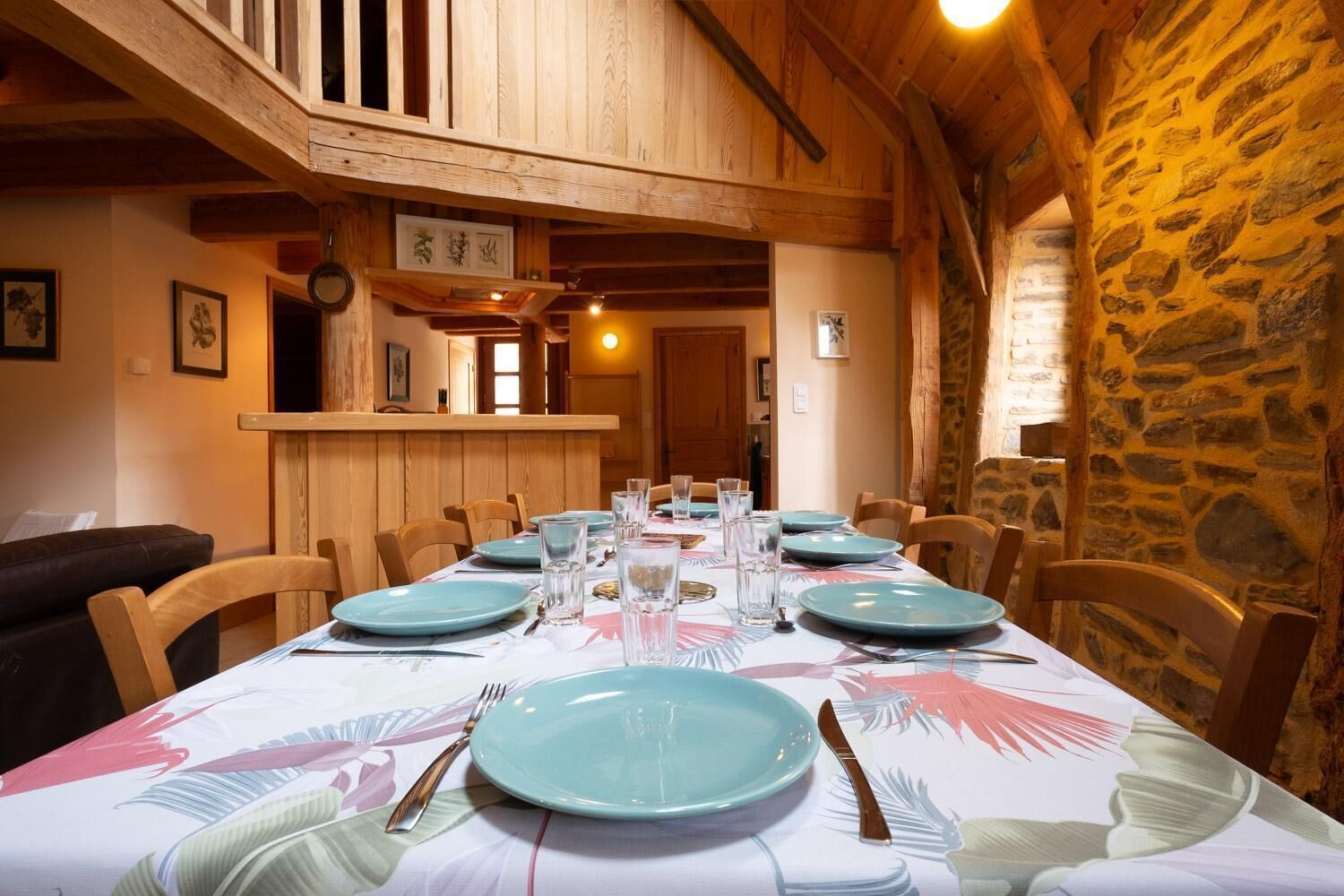 A dining area with a long table set for a meal, wooden chairs, and a stone wall.