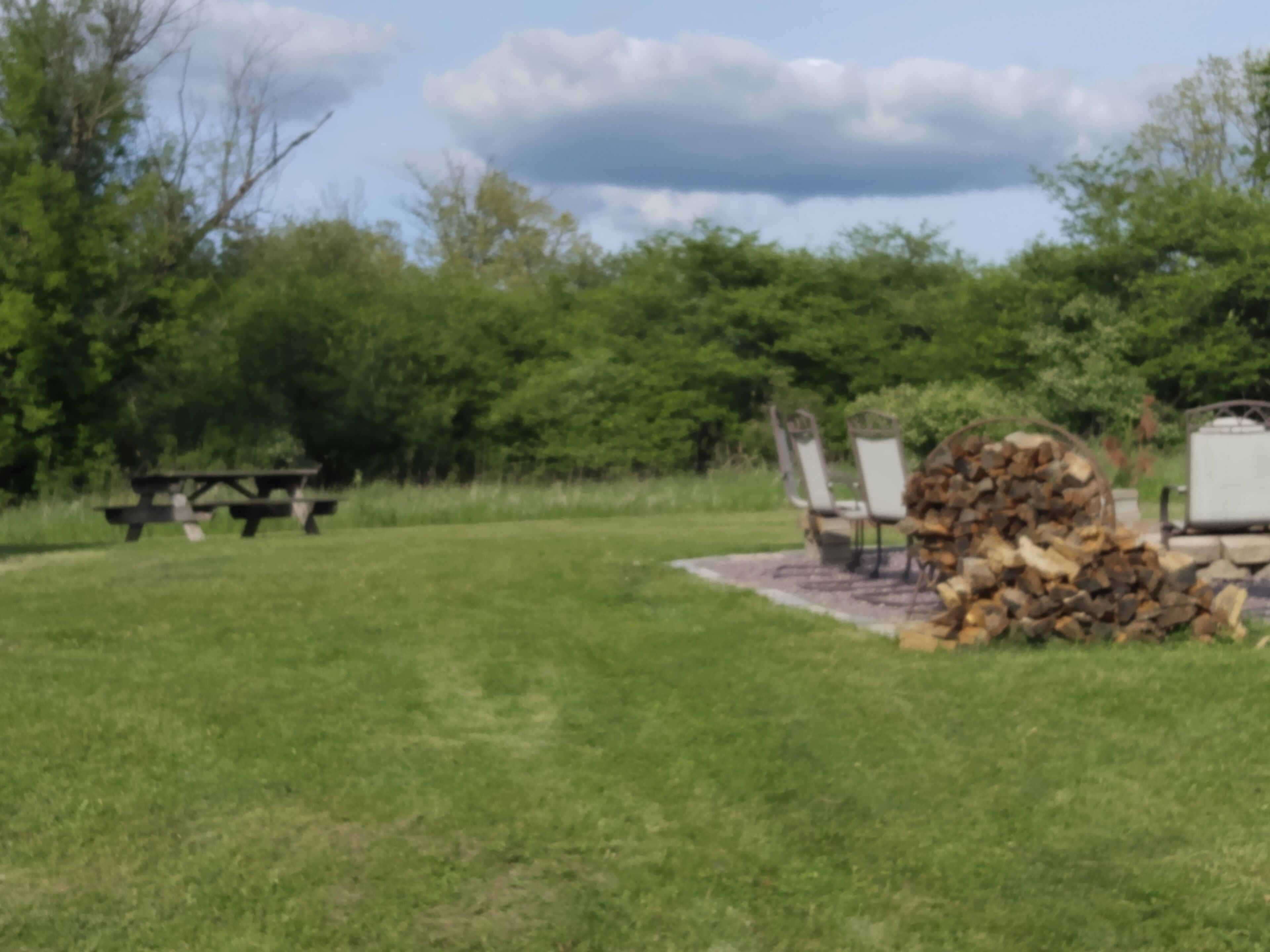 Un espace pique-nique équipé d’une table et de chaises, d’une pile de bois de chauffage et d’un foyer en pierre.